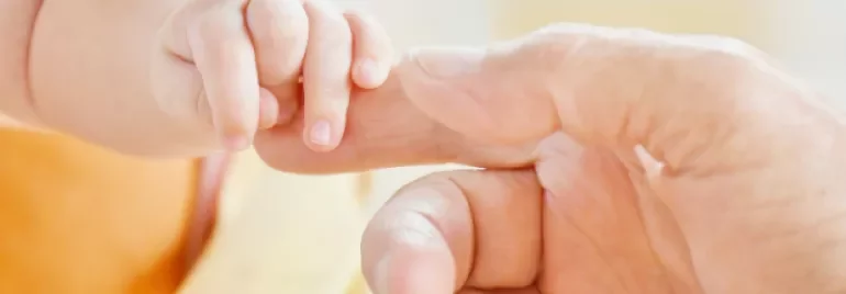 Adult hand gently holding a small child's hand.