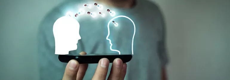 Person holding a smartphone projecting two glowing head outlines exchanging data.
