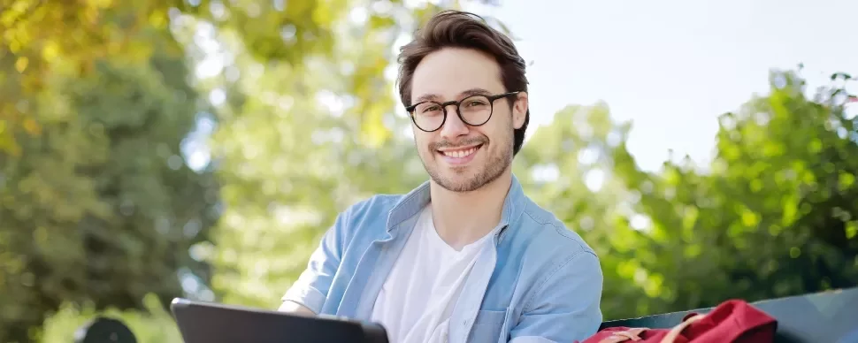 Person sitting outdoors smiling with a tablet.