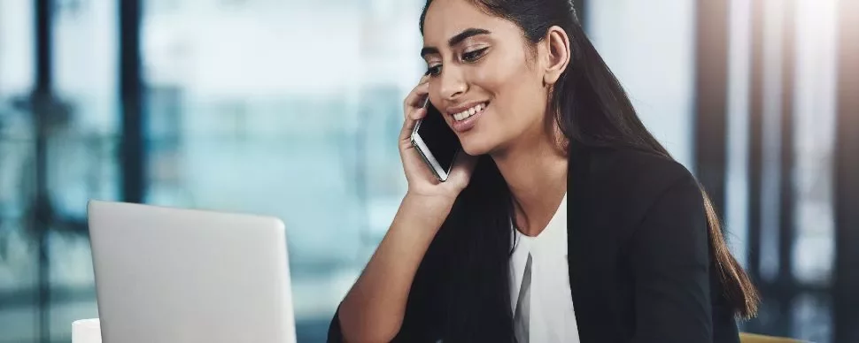 Person smiling while talking on a phone and using a laptop.
