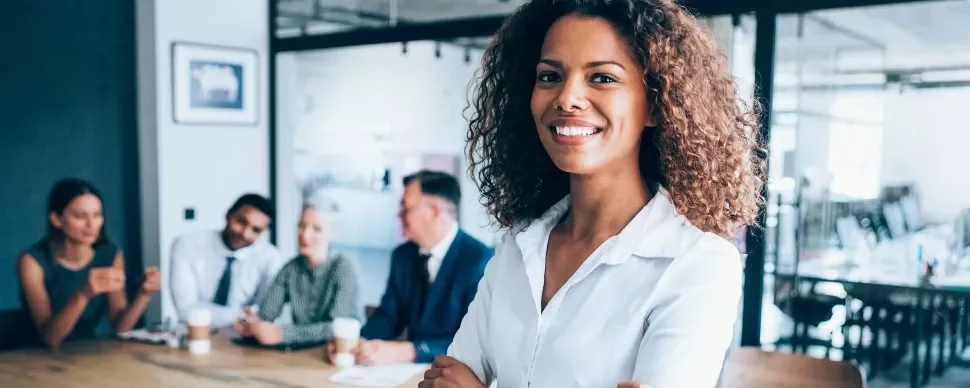 Smiling person standing in a modern office with colleagues in the background.