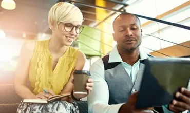 Two people sitting on stairs, smiling at a tablet.