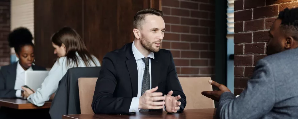 Two people in formal attire having a conversation at a table.