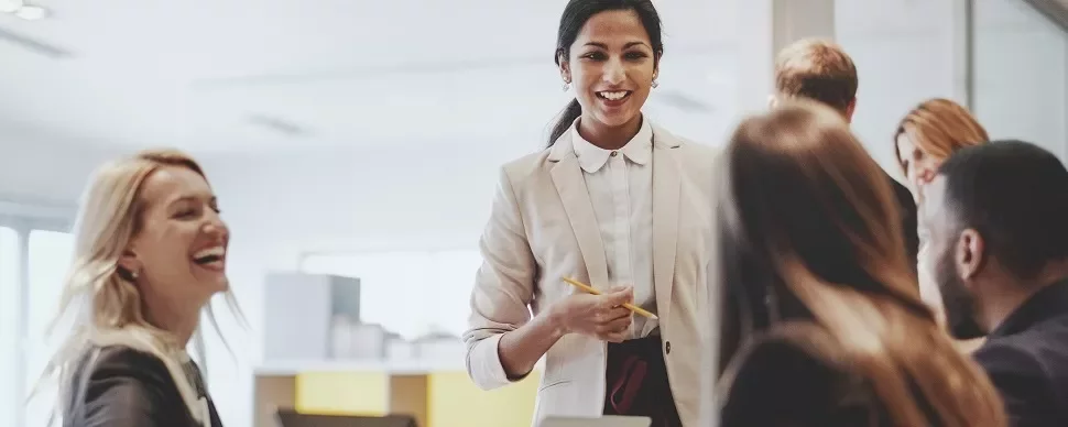 Group of people having a meeting in an office, one person standing and speaking.