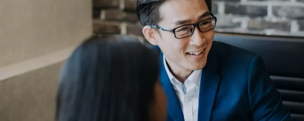 Person in a blue suit smiling during a conversation indoors.
