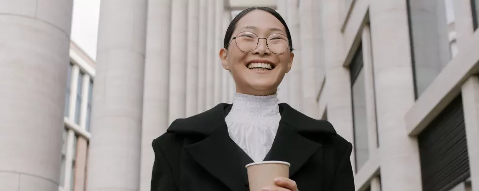 Person smiling with a coffee cup, standing in front of tall columns.