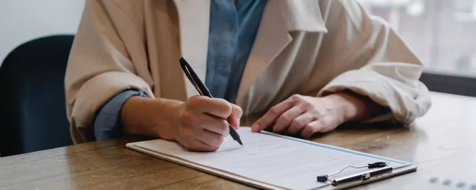 Person signing a document at a wooden desk with a pen.