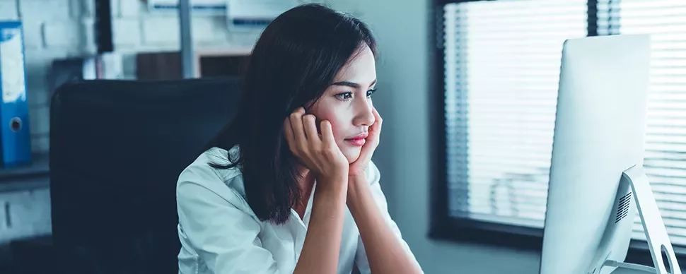 Person seated at a desk, looking intently at a computer screen in a modern office.