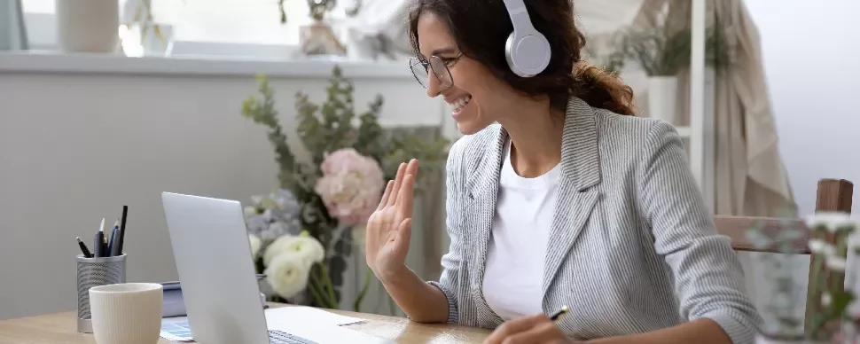 Person smiling while on a video call with headphones at a home office desk.