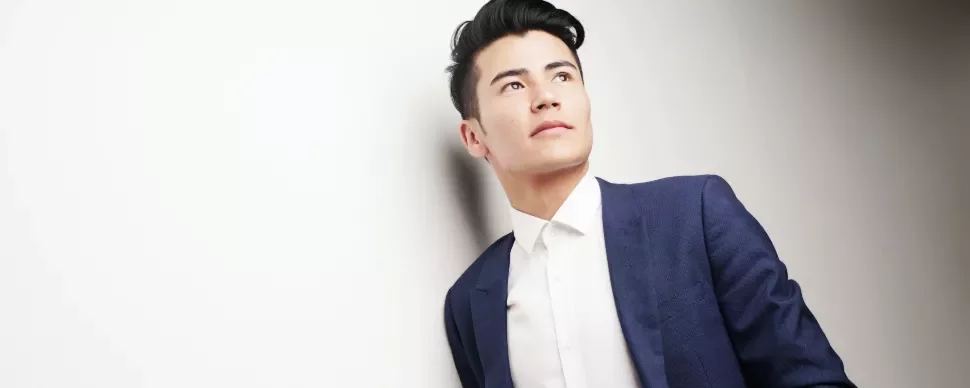 Person in a blue suit and white shirt looking upward against a light background.