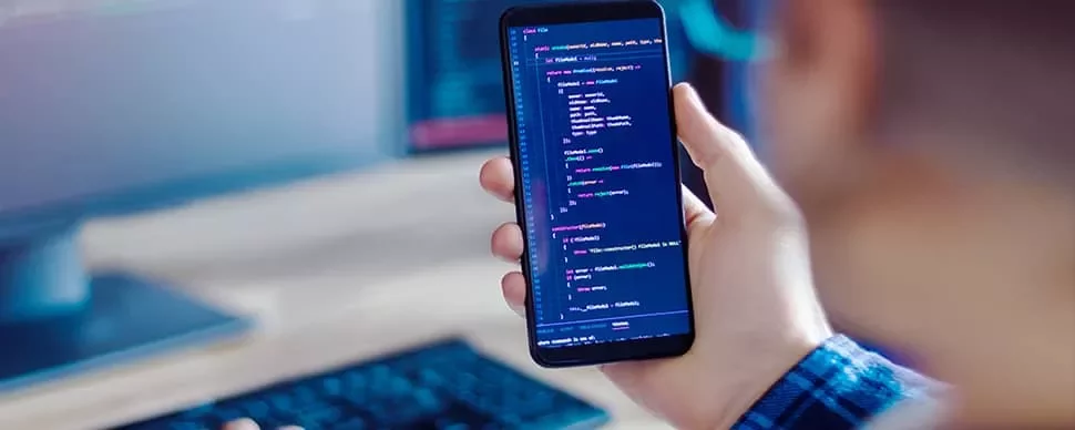 Person holding a smartphone displaying lines of code on the screen.