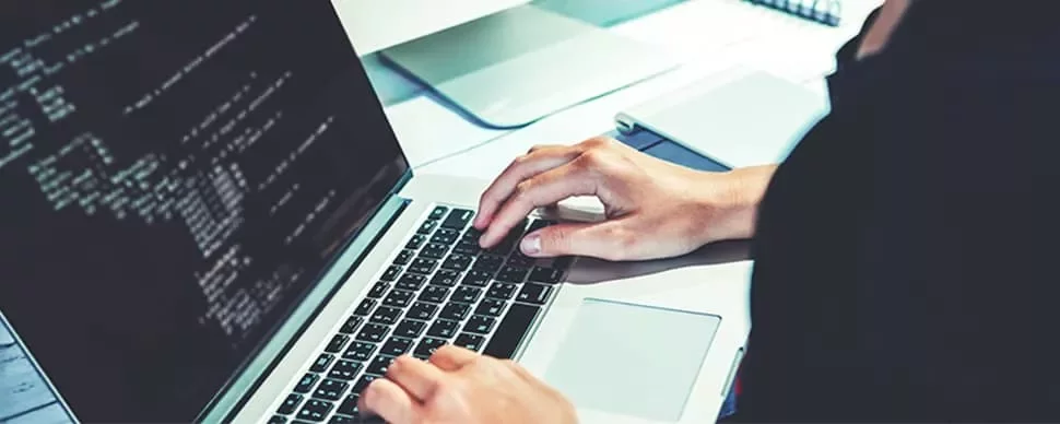 Person typing on a laptop with code on screen.