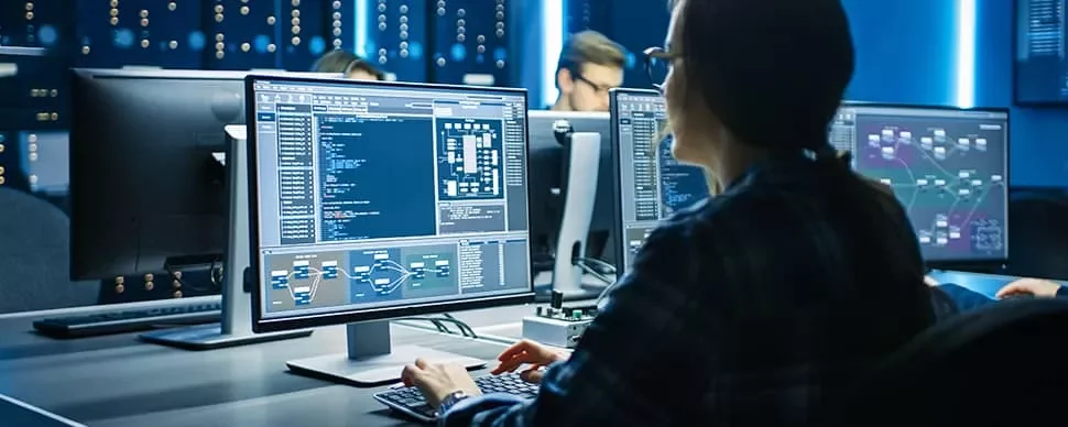 Person working at a computer with multiple monitors displaying code in a dimly lit office.