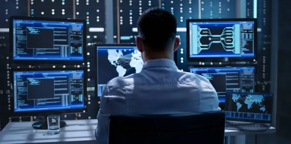 Person working with multiple digital screens in a control room.