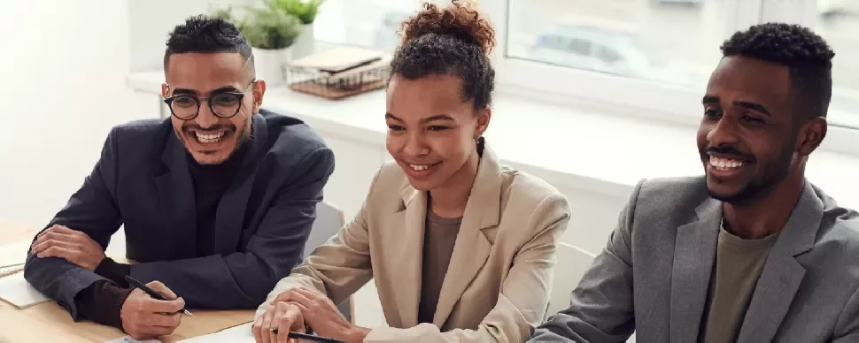 Three people smiling during a meeting at a table.