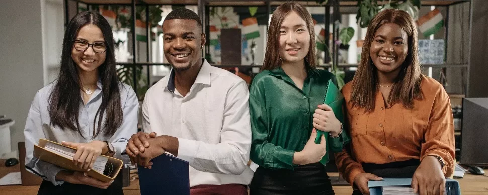 Four people smiling in an office setting, holding folders.