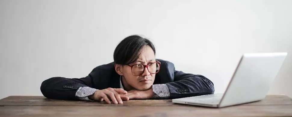 Person with glasses looking intently at a laptop on a wooden table.