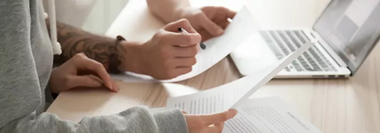 People reviewing documents at a desk with a laptop.