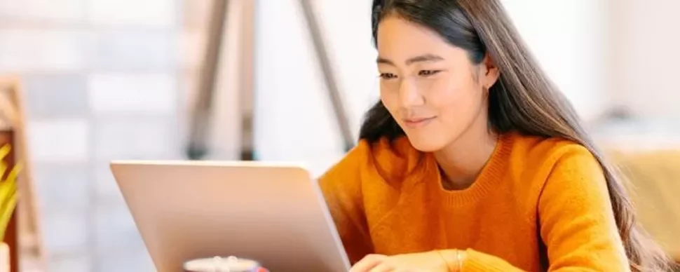 Person in orange sweater smiling while using a laptop.