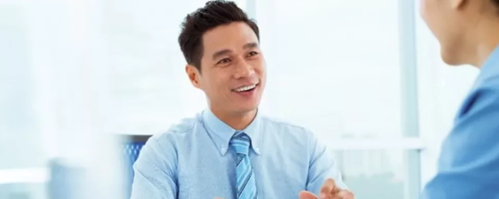 Person in a blue shirt smiling during a conversation in an office.