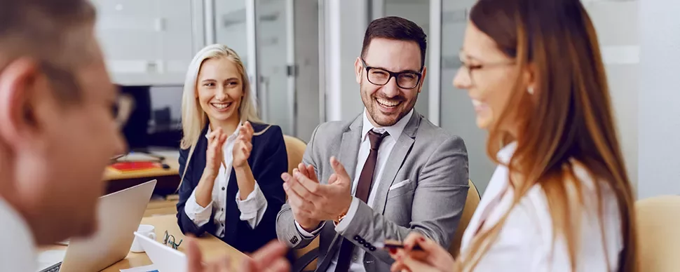 Group of professionals smiling and clapping in a meeting room.