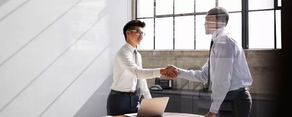Two people shaking hands in a bright office setting.