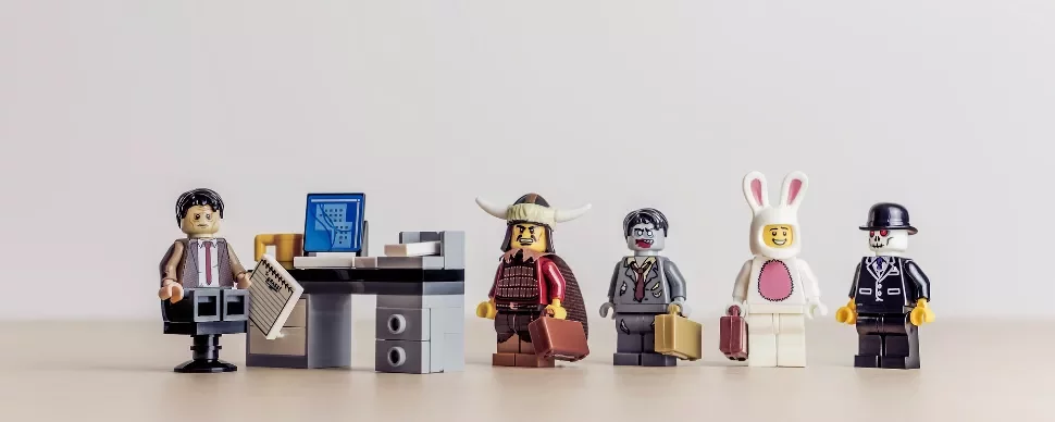 Lego figures in costumes wait in line by a small office desk.