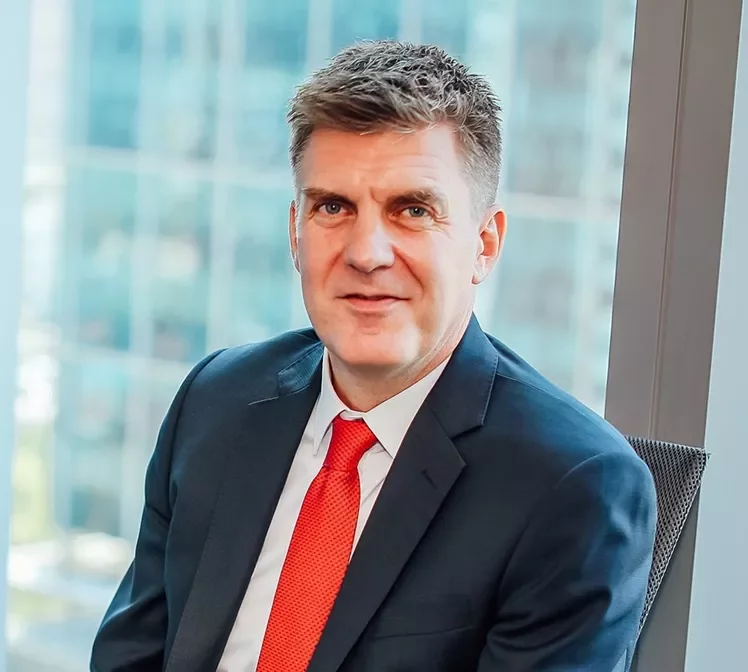 Smiling person in a suit and red tie by a window.