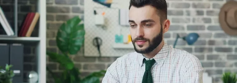 Person in an office setting with a brick wall and plants in the background.