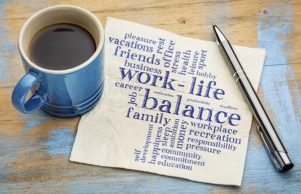 Coffee cup and pen next to napkin with words about work-life balance.