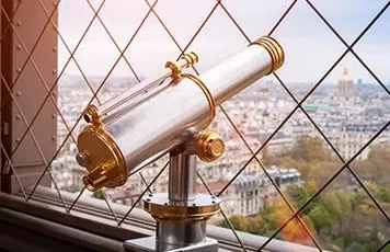Telescope on a platform overlooking a cityscape with a grid fence.