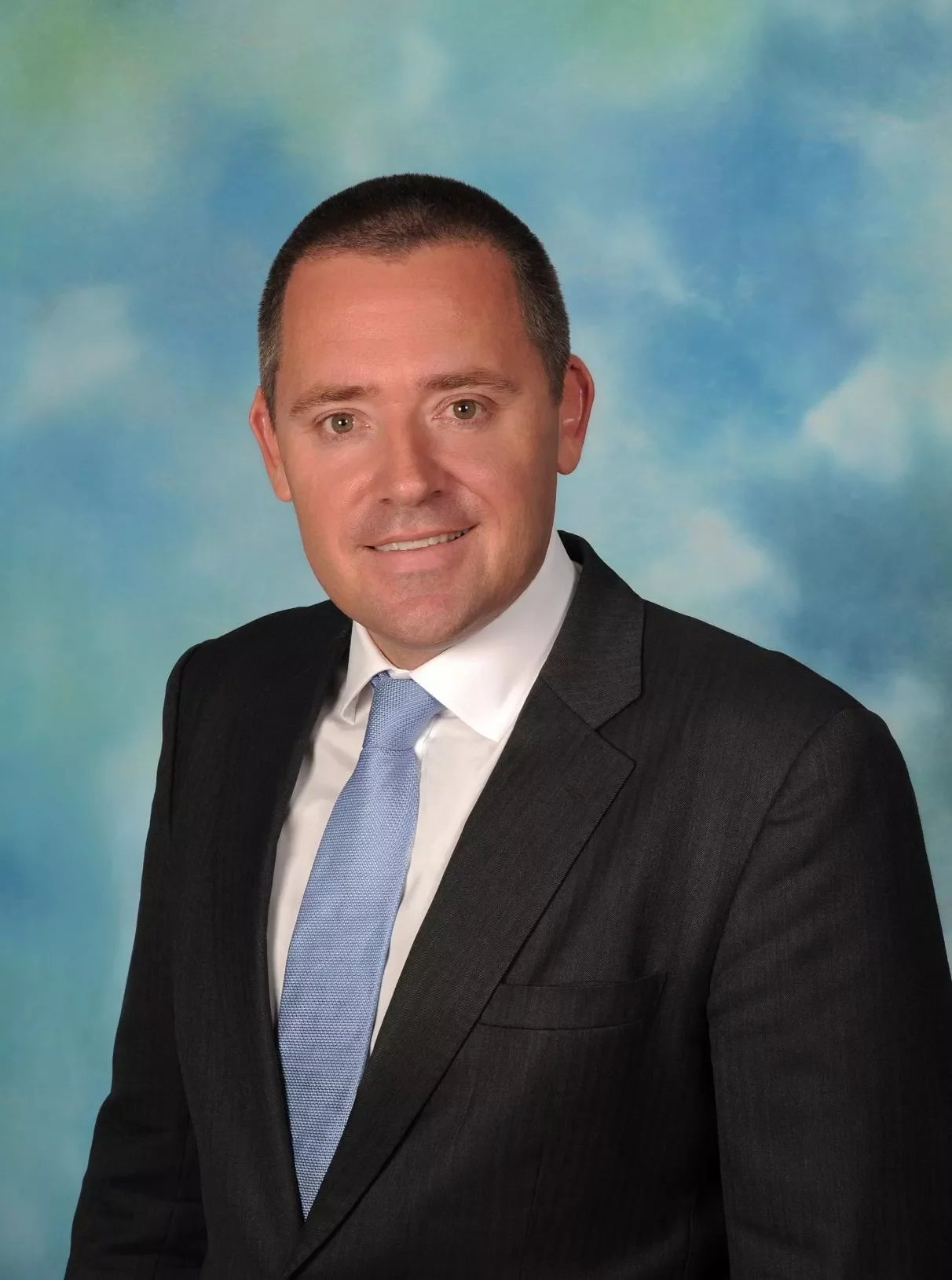 Professional headshot of a person in a suit and tie with a blue background.