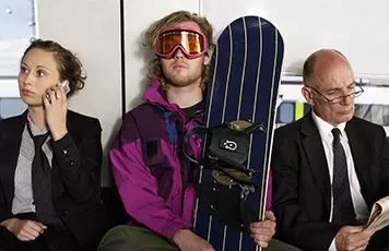 Three people sit on public transport, one holding a snowboard.