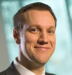 Person in a suit smiling with a blurred background.