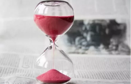 Red sand flows through an hourglass on a newspaper background.