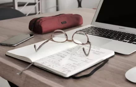 Notebook with glasses, pencil case, and a laptop on a wooden desk.