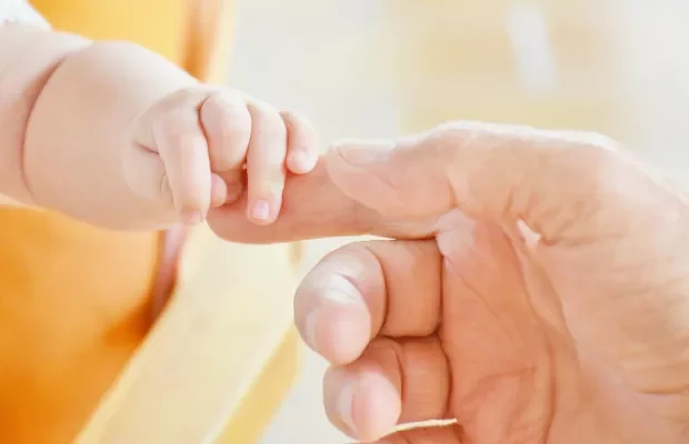 Adult hand gently holding a small child's hand.