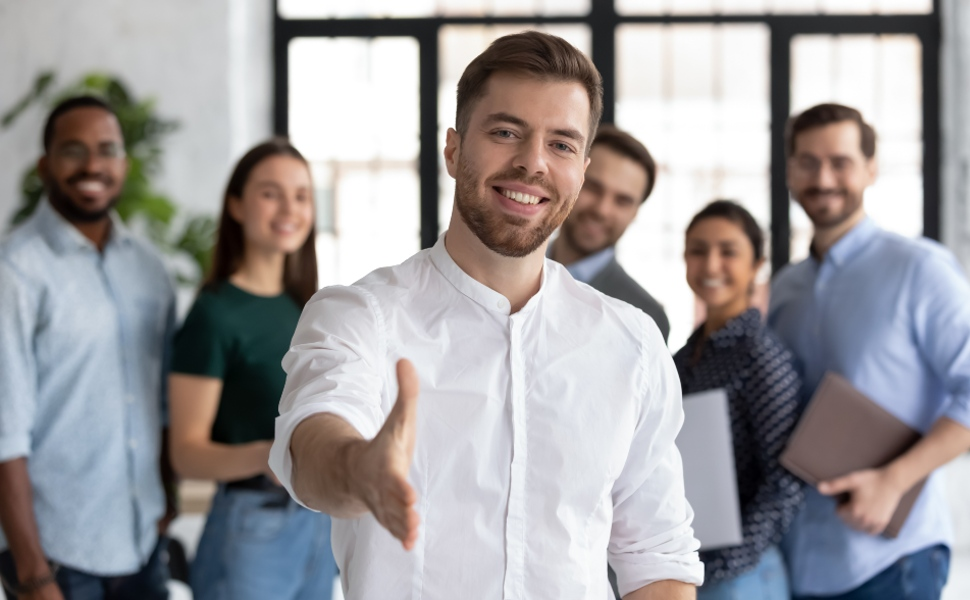 A group of white-collar professinals smiling and greeting a new joiner.